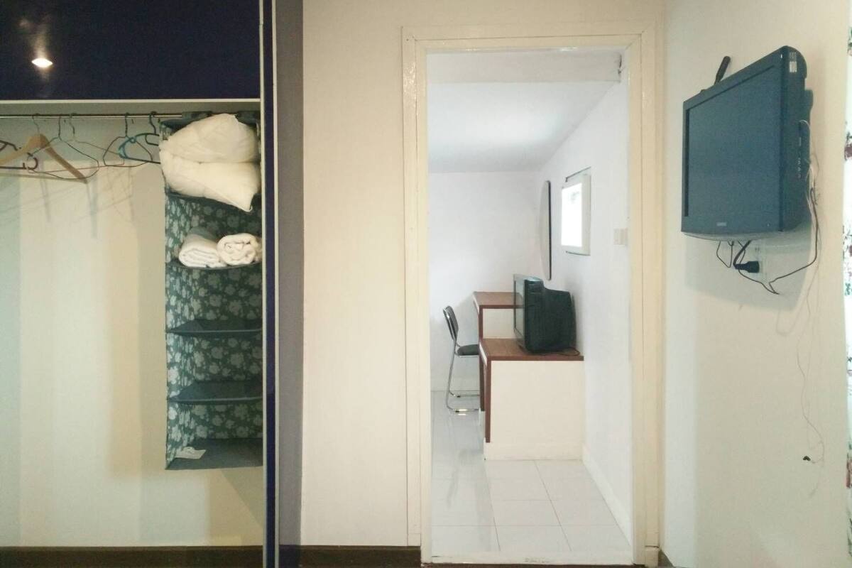 A room with a bed, a wardrobe, a desk with a chair, and a television mounted on the wall.