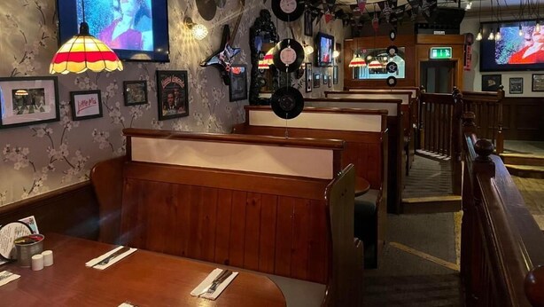 A restaurant with wooden booths, a bar area, and a television screen displaying a program. - The White Hart Hotel (Holsworthy)
