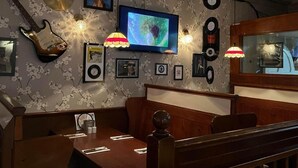 A restaurant interior with a wooden table, chairs, a television, wall decorations, and a ceiling with exposed wiring. - The White Hart Hotel (Holsworthy)