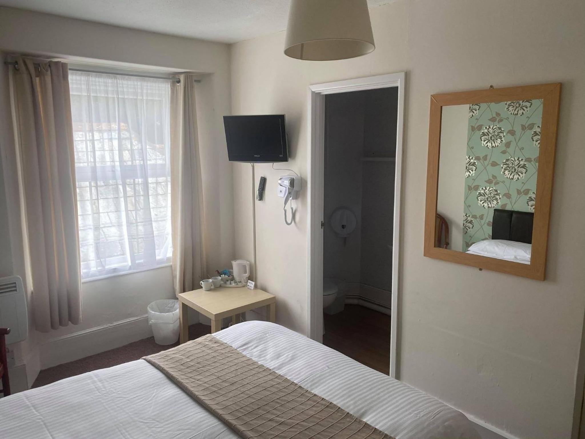 A hotel room with a bed, a television, a telephone, a small table with a coffee maker, and a bathroom visible through an open door.