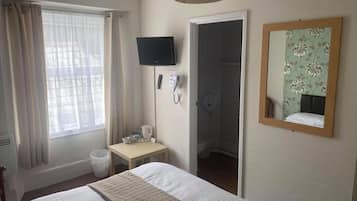 A hotel room with a bed, a television, a telephone, a small table with a coffee maker, and a bathroom visible through an open door.