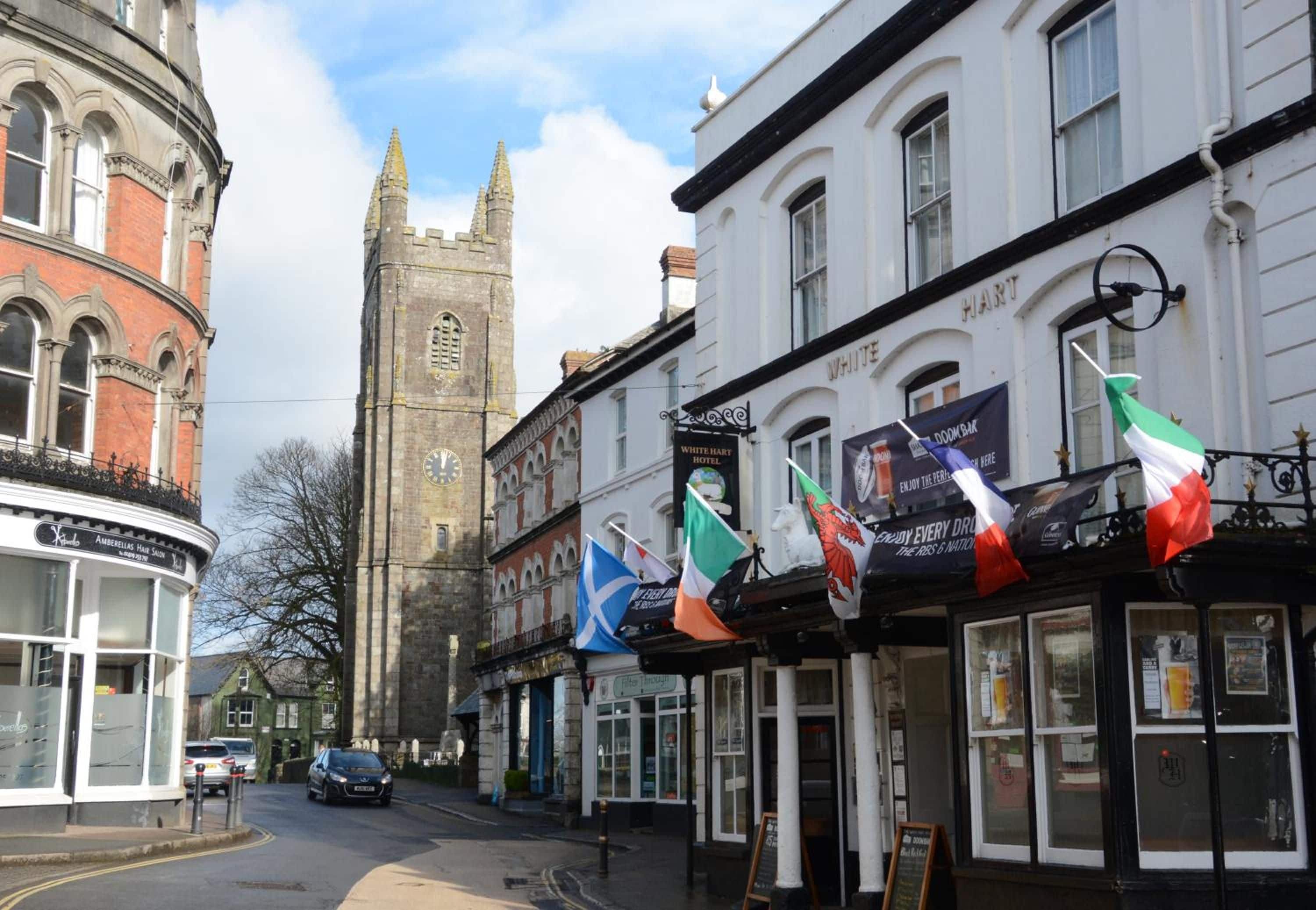 A street view with a historic building, a clock tower, and a pub with flags.