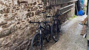 A narrow alley with a stone wall, a metal shelf, and two bicycles parked against the wall. - The White Hart Hotel (Holsworthy)