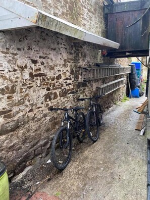 A narrow alley with a stone wall, a metal shelf, and two bicycles parked against the wall. - The White Hart Hotel (Holsworthy)