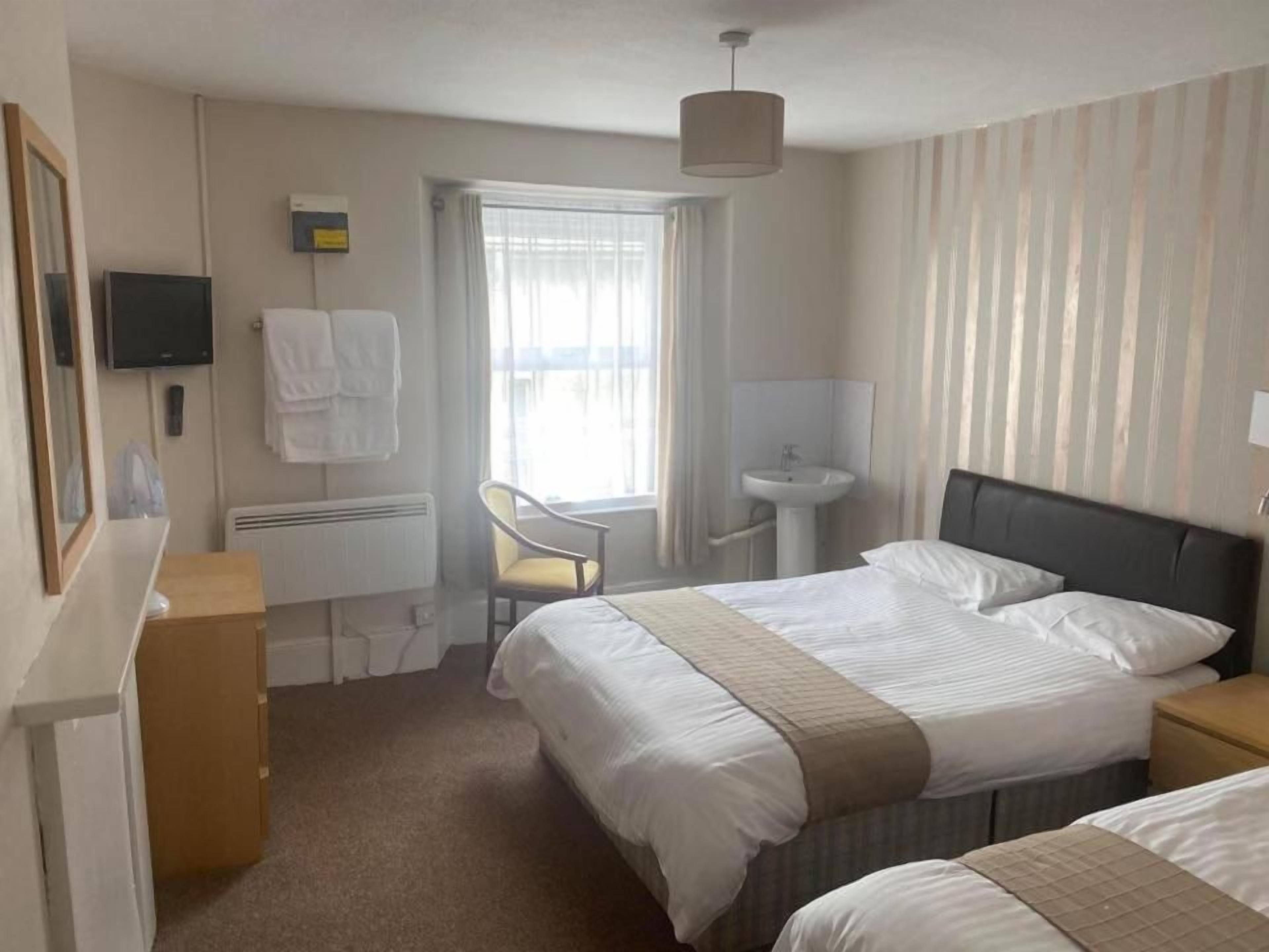 Habitación de hotel con cama, escritorio, silla, televisor y ventana con cortinas.