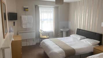Habitación de hotel con cama, escritorio, silla, televisor y ventana con cortinas.
