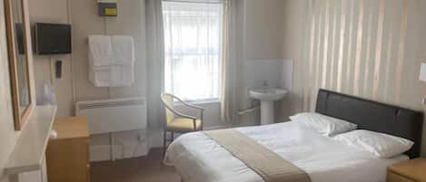 A hotel room with a bed, a desk, a chair, a television, and a window with curtains.