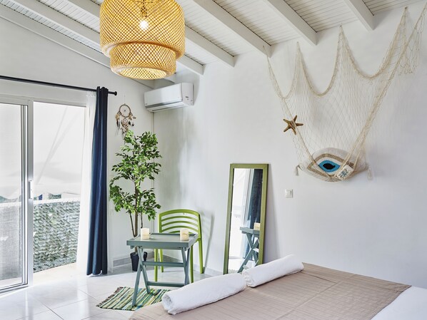 A modern room with a bed, a green chair, a table with candles, a potted plant, and a hammock.