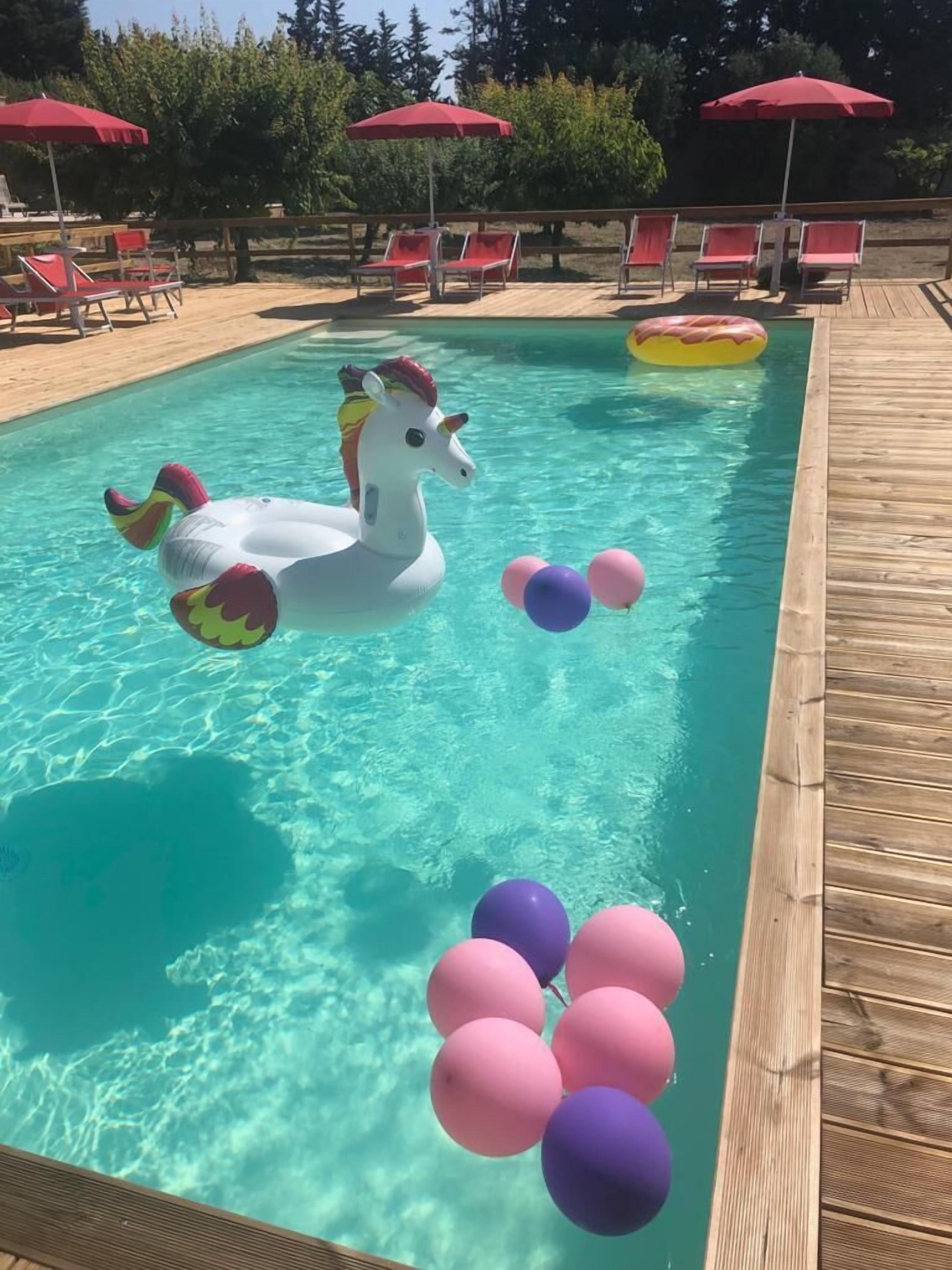 A swimming pool with inflatable unicorn floats and pink and purple balloons.