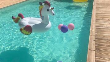 A swimming pool with inflatable unicorn floats and pink and purple balloons.