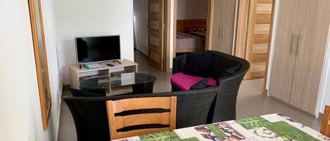 A compact living space with a dining table, a television, and a wicker chair.