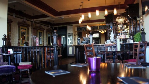 A bar area with wooden furniture, a bar counter, and hanging lights. - The Royal (Morecambe)