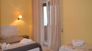 Una habitación de hotel con cama, mesita de noche, lámpara y una puerta con cortinas.