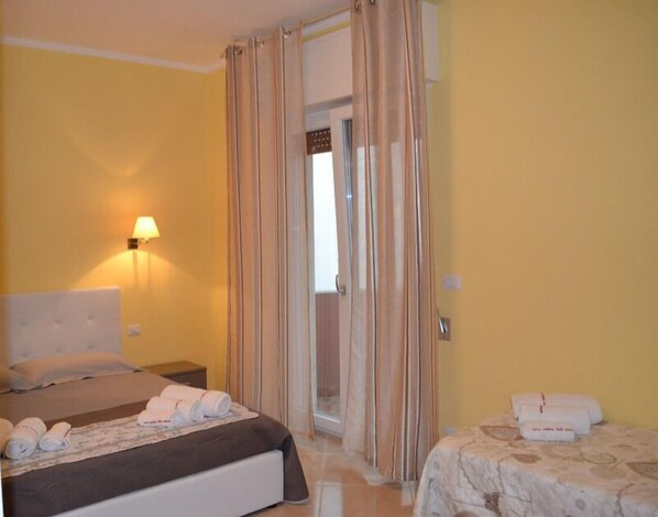 A hotel room with a bed, a nightstand, a lamp, and a door with curtains.