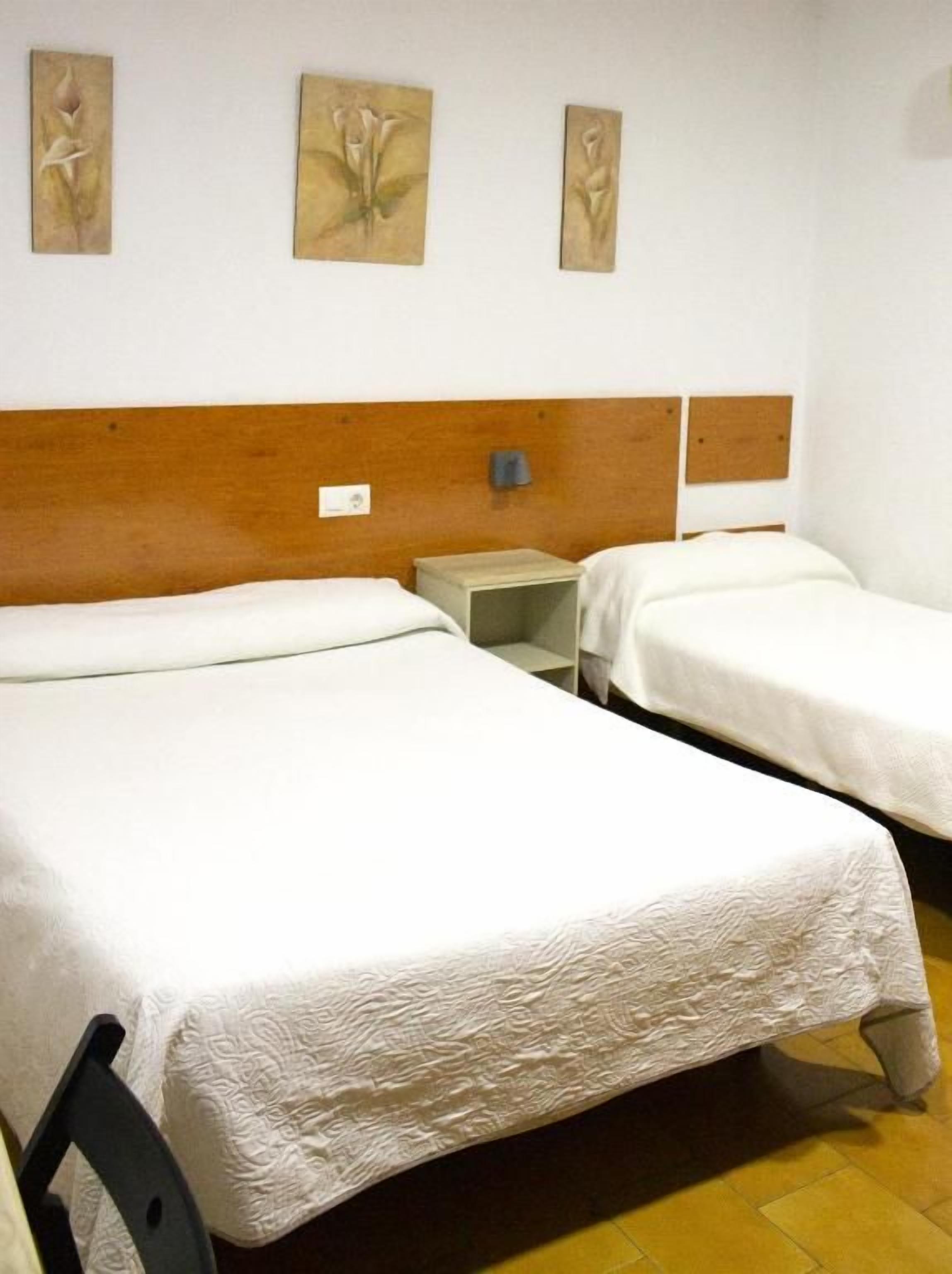 Habitación de hotel con dos camas individuales, cabecera de madera, mesita de noche y una obra de arte colgada en la pared.