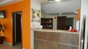 A reception area with a counter, a television mounted on the wall, a potted plant, and a fire alarm. - Hostal Villa (Chiclana de la Frontera)