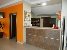 Un área de recepción con mostrador, un televisor montado en la pared, una planta en maceta y un detector de incendios.