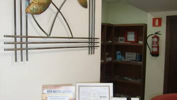 A reception desk with a metal wall art piece, a sign for a cafeteria, and a fire extinguisher.