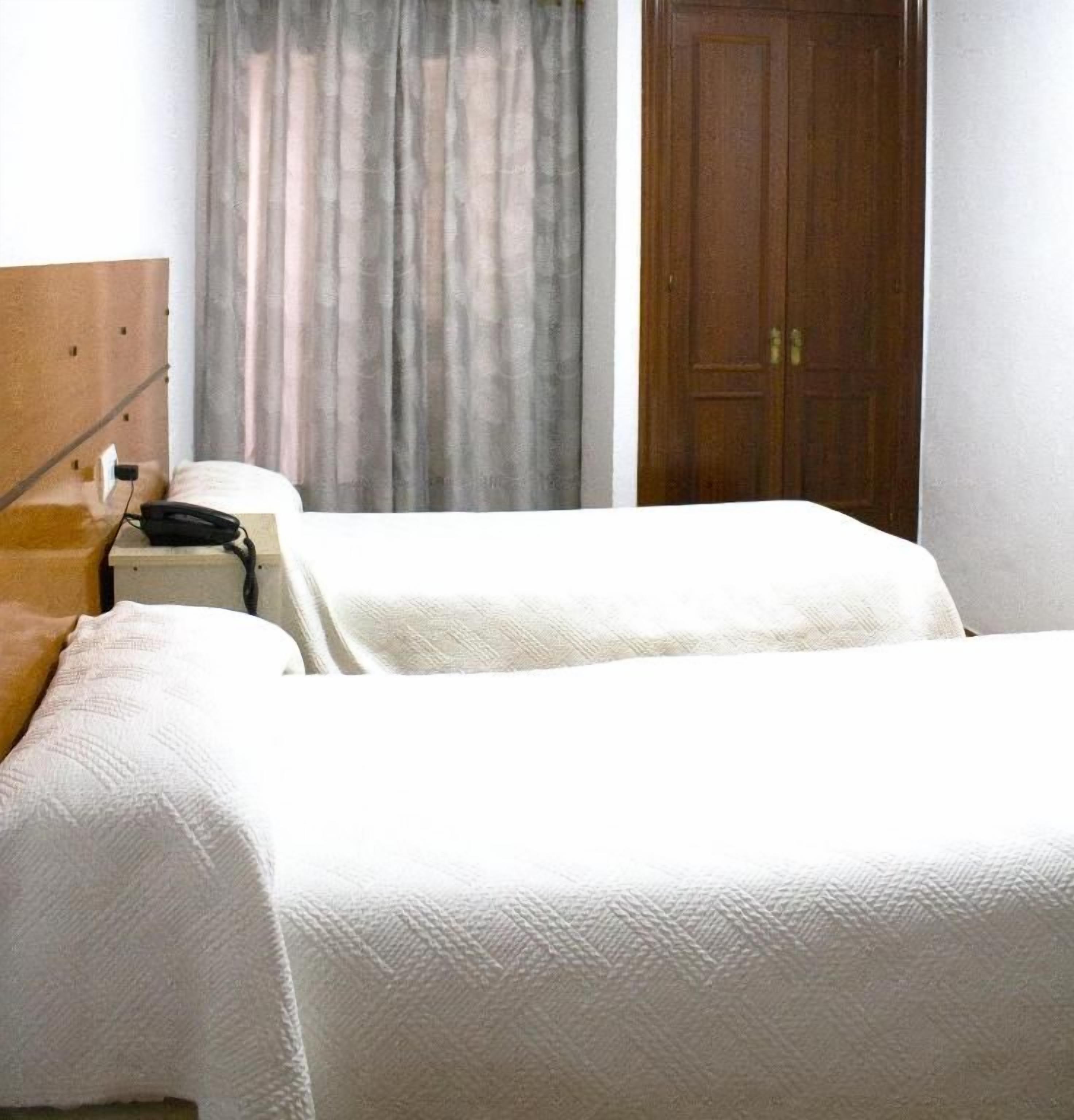 Een hotelkamer met twee bedden, een houten hoofdbord, een nachtkastje en een gesloten deur.