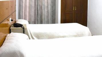 A hotel room with two beds, a wooden headboard, a nightstand, and a closed door.