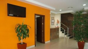 A lobby with orange walls, a flat-screen TV mounted above a door, and two potted plants. - Hostal Villa (Chiclana de la Frontera)