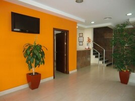 Un vestíbulo con paredes anaranjadas, un televisor de pantalla plana sobre una puerta y dos plantas en macetas.