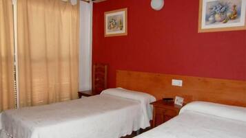 A room with two beds, a wooden headboard, a small table, and a wall-mounted air conditioner.