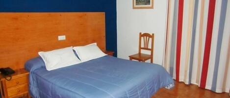 A bedroom with a wooden headboard, a bed with blue bedding, a wooden nightstand, a chair, and a striped curtain.