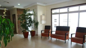 A spacious lobby with a large window, two potted plants, and three patterned armchairs. - Hostal Villa (Chiclana de la Frontera)