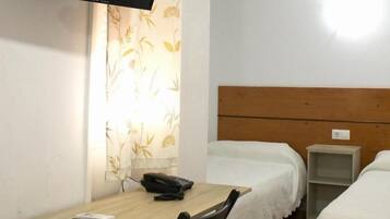 Una habitación con cama, escritorio, silla, televisor montado en la pared y una pequeña estantería.