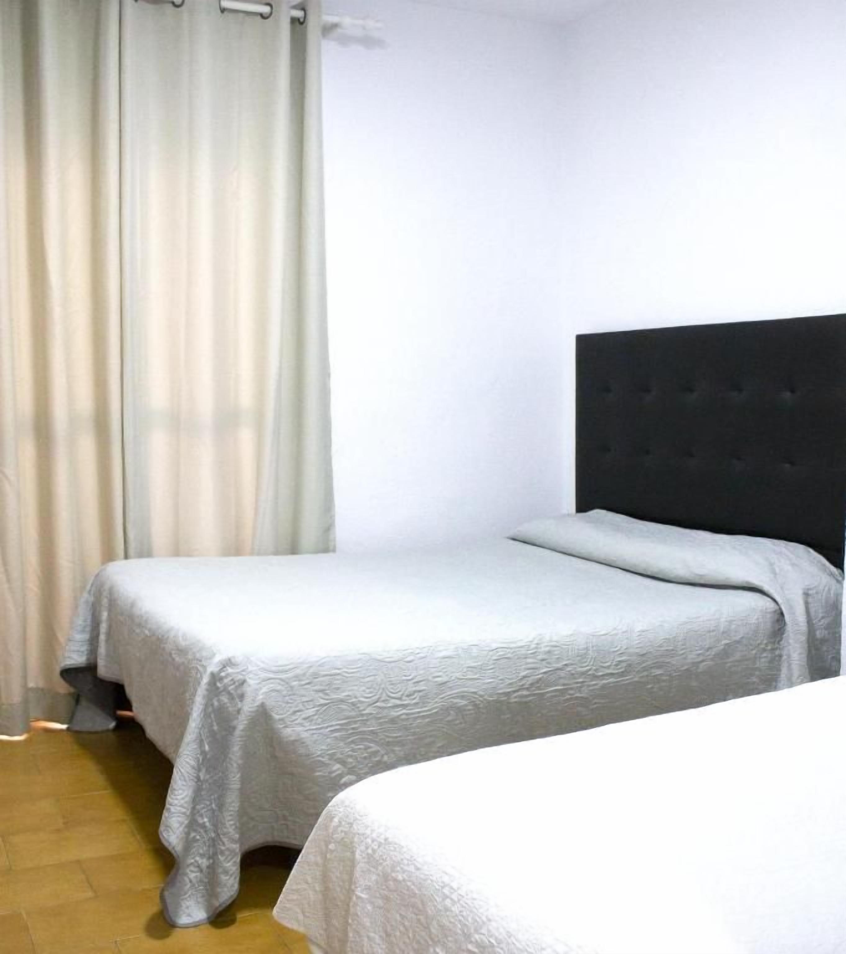 Une chambre avec deux lits, une tête de lit sombre et un rideau.