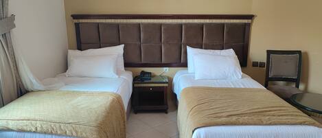 A hotel room with two beds, a nightstand, a small table, and a painting of camels on the wall.