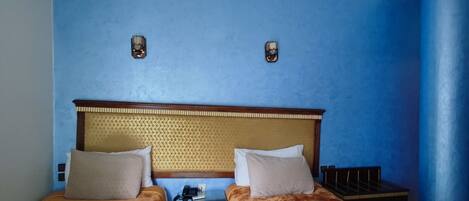 A hotel room with two beds, a wooden headboard, a nightstand, and a blue wall.