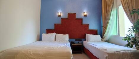Habitación de hotel con dos camas, cabecera roja, mesita de noche, lámpara de pared y ventana con cortinas.
