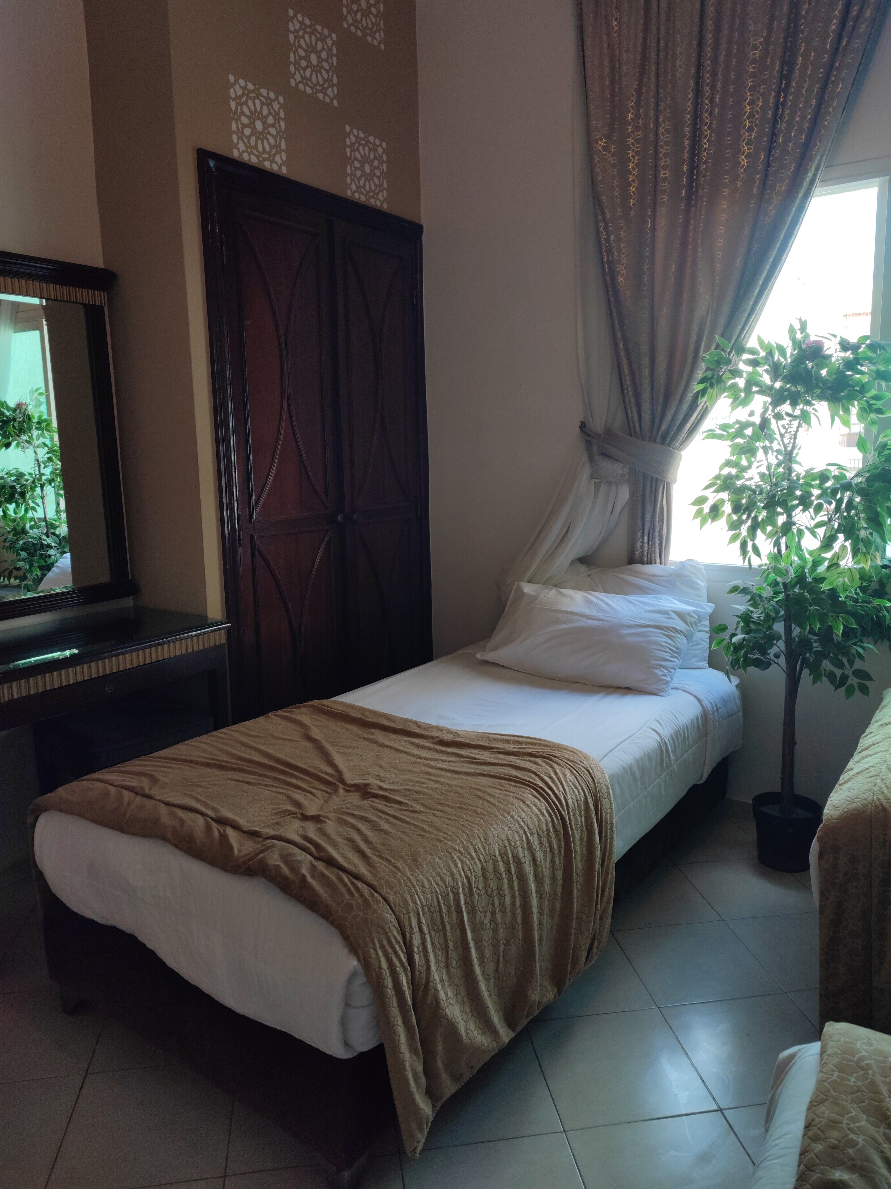 A bedroom with a bed, a dresser, a mirror, a window with curtains, and a potted plant.