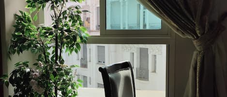 Una habitación con una planta en maceta, una silla y una mesa cerca de una ventana con cortinas.