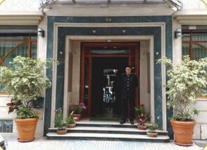 Entrada de edifício com o número '59' sobre a porta, ladeada por vasos de plantas.