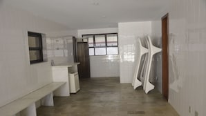 Une salle de bain avec des murs recouverts de carreaux blancs, un banc, un lavabo et une fenêtre avec des rideaux.
