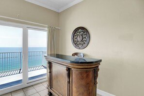 A room with a wooden cabinet, a wall clock, and a sliding glass door leading to a balcony with a view of the sea.