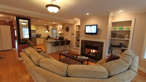 A living room with a large beige sectional sofa, a fireplace, and a television mounted on the wall. - Vintage charm with open concept floor plan, great for entertaining and families. (Chicago)