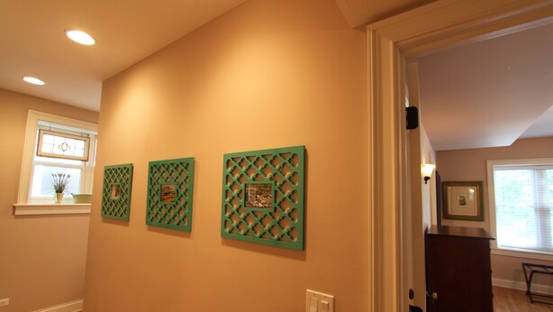 A hallway with three green decorative panels on the wall, a window with a vase of flowers, and a wooden floor. - Vintage charm with open concept floor plan, great for entertaining and families. (Chicago)