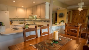 Una cocina con armarios blancos, una estufa y un comedor con mesa y sillas de madera.