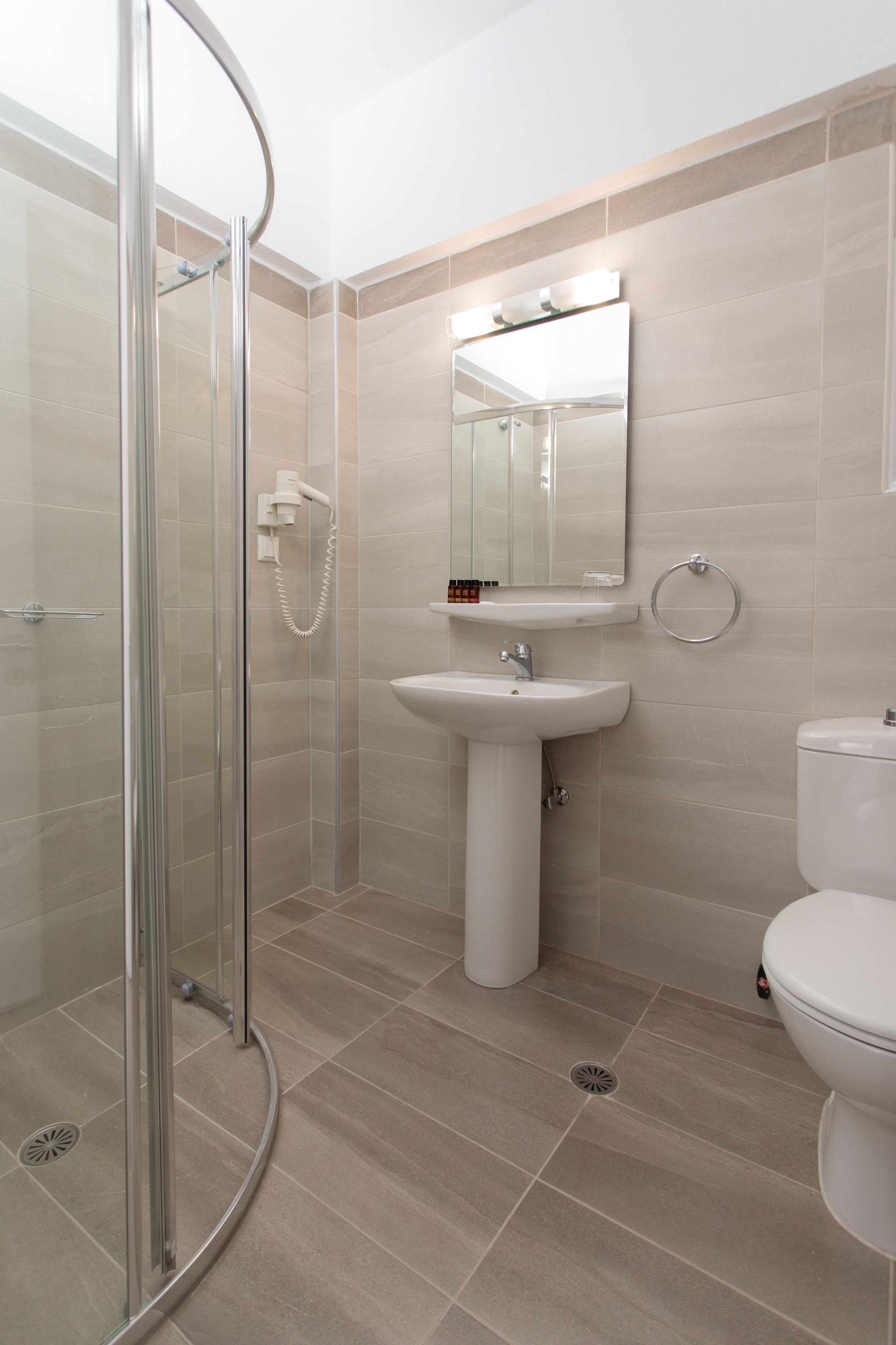 Une salle de bain avec une douche à parois de verre, un lavabo sur colonne, des toilettes et un miroir avec des lumières au-dessus.