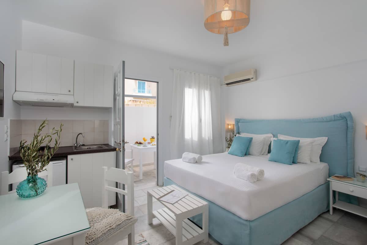 Un dormitorio con cama, mesitas de noche, una pequeña mesa con silla, ventana con cortinas y vistas al exterior.