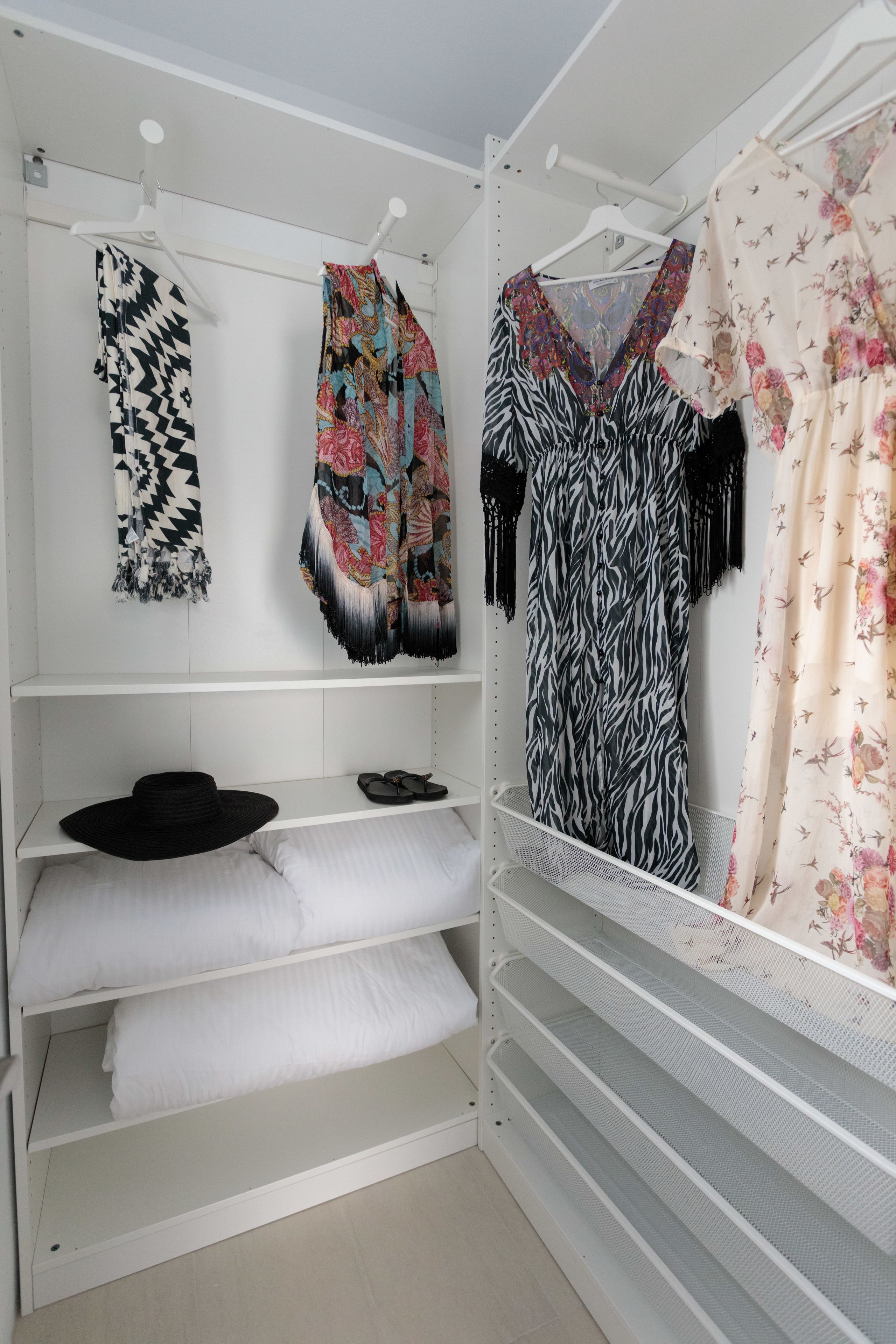 Vestidor amplio con estantes y espacio para colgar ropa, mostrando vestidos estampados y un sombrero negro.