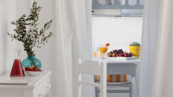 Una mesa de comedor blanca con un frutero, un vaso de jugo de naranja y una planta en maceta.