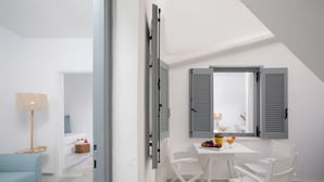 A modern, well-lit room with a dining area featuring a table and chairs, a sofa, and a lamp. - Ippokampos Town Apartments (Naxos)