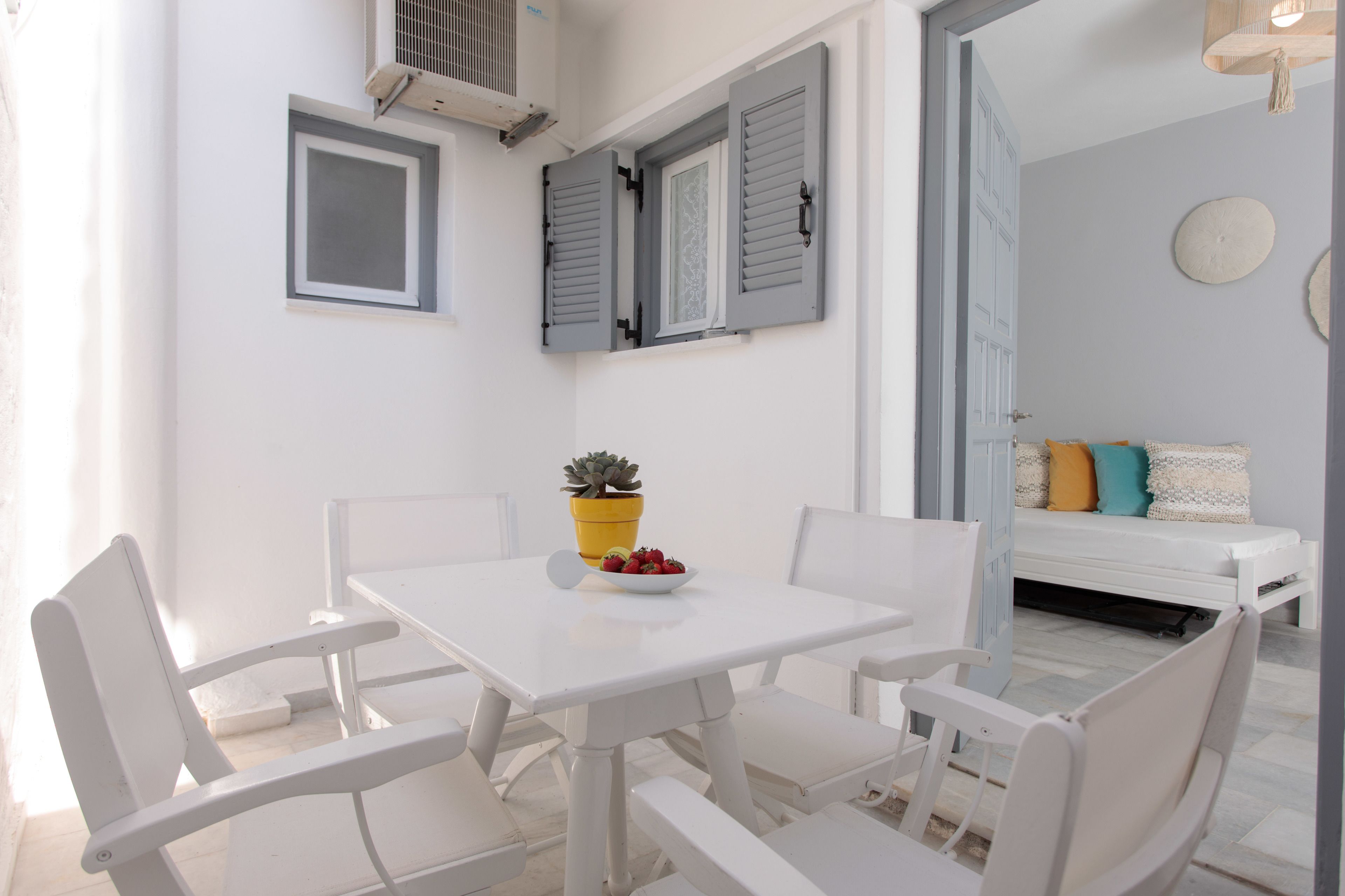A white dining table with four chairs, a small potted plant, and a bowl of fruit.