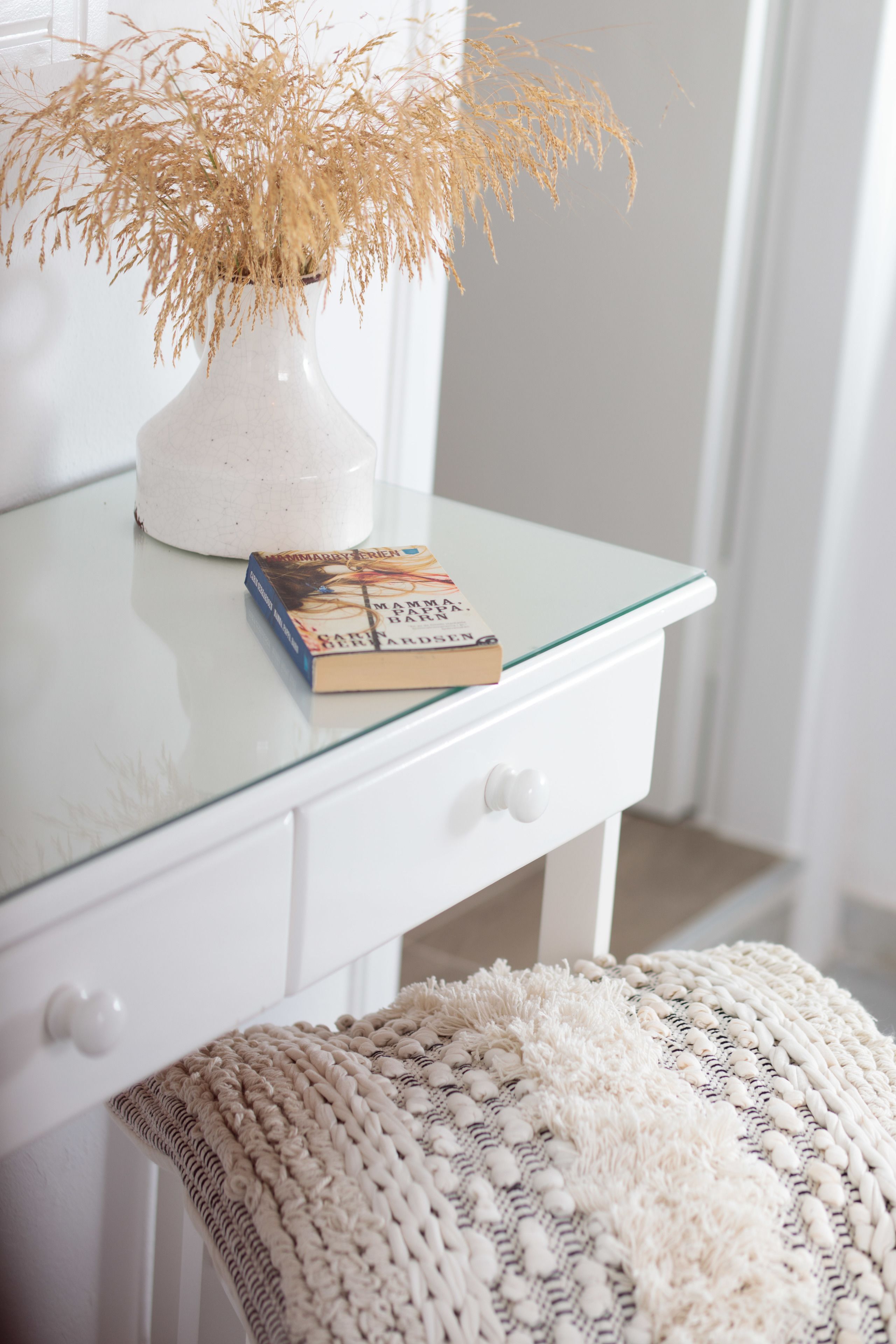 A white desk with a glass top, a white vase with dried plants, and a book titled "Mammals, Birds, and Reptiles" by David Burnie.