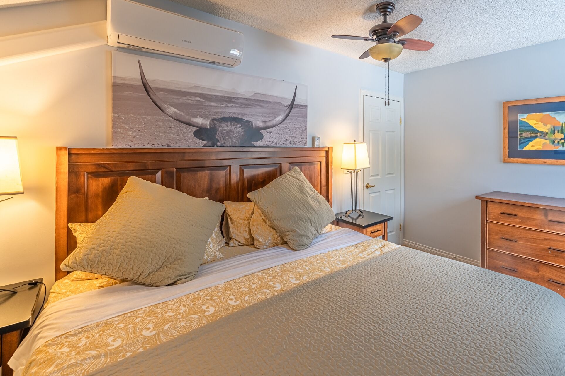A neatly made bed with a wooden headboard, two bedside lamps, and a ceiling fan.
